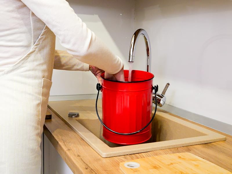 Red compost bin being washed in kitchen sink