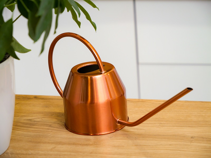 Rose gold metal watering can with long spout on wooden table