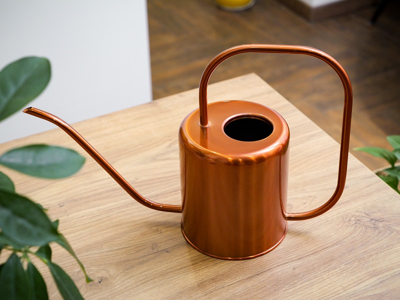 Rose gold watering can displayed on a wooden table